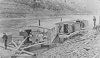 Three Arks for a log drive on Pine Creek, in Lycoming or Tioga County, Pennsylvania. The left ark was for cooking and dining, the middle ark was the sleeping quarters and the right ark was for the horses. The arks were built for just one log drive and then sold for their lumber. The line of the Jersey Shore, Pine Creek and Buffalo Railway can be seen on the eastern shore: the mountainside behind it is nearly bare of trees from clearcutting.[6]