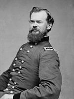 Black and white photo of a bearded man sitting and leaning backward. He wears a dark military uniform with two rows of buttons and the two stars of a major general on the shoulder tabs.