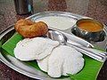 The South Indian staple breakfast item of idli, sambar, and vada served on a banana leaf. Note the stainless steel plates and cups; characteristic of south Indian dining tables.