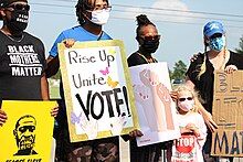 Protesters along funeral procession wearing COVID mass and holding signs