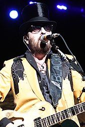 A color photograph of David A. Stewart, who is singing while wearing a golden tuxedo.