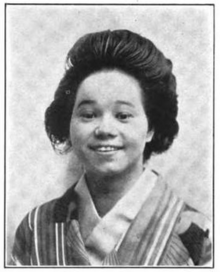 A smiling young Japanese-American woman, with dark hair in a bouffant style, wearing a striped kimono