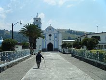 A person walks down a street in Joquicingo de León Guzmán with a church in the background.