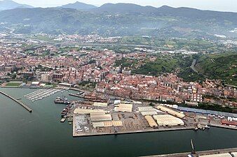 Aerial view of the industrial port and city of Santurtzi with green mountains in the background and ocean in the foreground