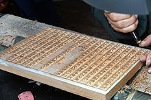 A photo of a person carving Chinese characters into a row of wooden blocks