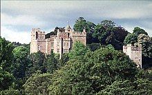 Upper sections of castle walls and towers showing above trees.