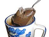 A tea bag being removed from a mug of hot tea to stop the brewing process