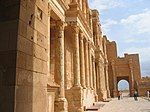 A side view of a large building to the right, with stone, cylindrical pillars running along its front.