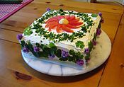 Smörgåstårta with cream-cheese icing and chives, boiled egg yolk, wood-sorrel leaves, tomatoes and flowers for decoration