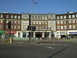 A brown-bricked building with white columns and a sign reading "HENDON CENTRAL STATION" in blue letters all under a clear, blue sky