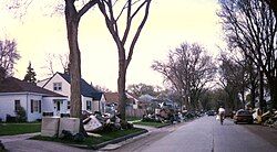 A neighborhood with piles of damaged possessions located in front of many homes. The piles included a washer and dryer, mattresses, and furniture. A man can be seen riding a bike down the middle of the street.