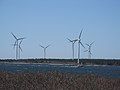 Seven three-blade wind turbines on the shore. A fishing boat is passing by.