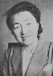 A middle-aged Japanese woman with dark hair, wearing a blouse and a tweed jacket