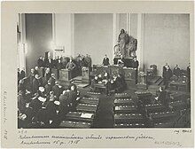 Parliament is convening for the first time after the war. White and German soldiers dominate the picture while only one person from the opposition social democrats is present. Thus, it was sarcastically called a Rump Parliament.