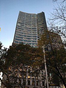 Northern facade of HSBC Tower as seen from Bryant Park at dusk, with trees in the foreground