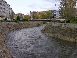 A river in Carballo, Spain with five story apartment buildings on both sides of the river.