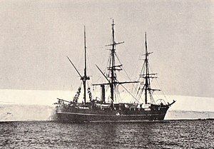 Three-masted ship with sails furled, lying next to a shelf of ice.