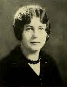 A young white woman wearing a dark top and dark beads