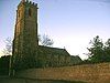 Stone building with square tower, partially obscured by trees.