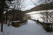 A snow-covered scene, lit by low sunlight, shows the footpath curving to the left before disappearing behind bare trees