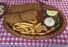 Two small versions of Karađorđeva šnicla served on a plate with fries, a bowl of tartar sauce, and lemon