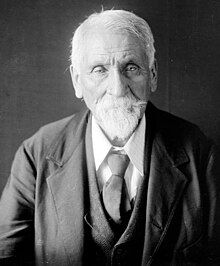 black and white portrait of Mathias Splitlog as an older man, with white hair and a trimmed white beard and moustache, and a three-piece suit