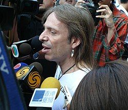 close-up of Alain Robert surrounded by microphones, appearing to speak