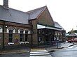 A brown-bricked building with a rectangular, dark blue sign reading "RUISLIP STATION" in white letters all under a clear, white sky