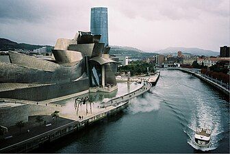 View of Bilbao, with the Guggenheim museum on the left of a river containing a motorboat