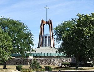 A modern church building with a green, domed roof, a glass tower above the roof, and brown arches above the tower