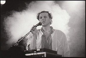 black-and-white image of Luboš Pospíšil standing in front of a control board onstage, holding a microphone, with smoke behind him