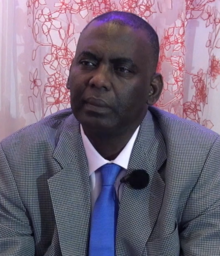 Biram Dah Abeid wearing a white shirt, blue tie, and grey blazer, looking intently just right of camera