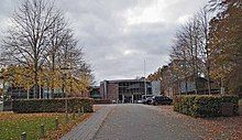 A building made of red bricks and glass, its access road with trees