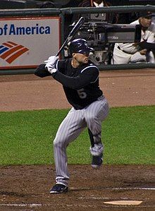 A man in a black baseball jersey and gray pinstriped pants prepares for a right-handed baseball swing.