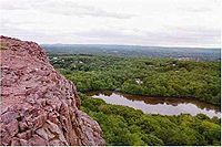 Vista of a rocky cliff overlooking a forest and pond