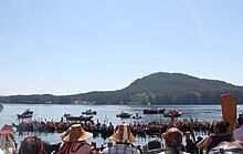 A crowd facing a lake with many canoes lined up.