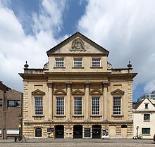 An imposing eighteenth-century building with three entrance archways, large first-floor windows and an ornate peaked gable end above.