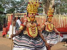 Two colourfully-dressed dancers with spears, masks and headdresses