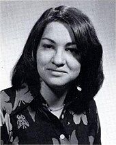 A formal pose of a young woman in her early twenties, dark straight hair parted near the center, wearing a dark floral print top.