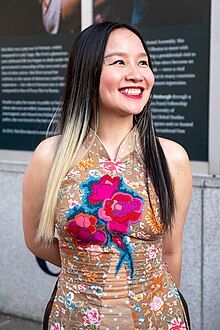 Mai Khôi wearing a traditional Vietnamese sleeveless dress, grinning and looking left of camera