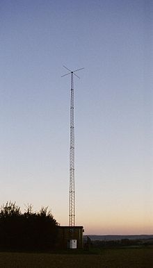 Tall antenna tower on a background of twilight clear sky; small shack is at bottom of tower