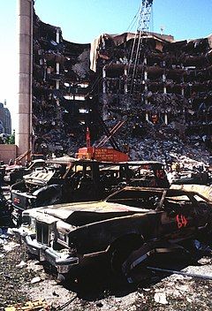 Several fire-damaged cars located in front of a partially destroyed multi-story building.