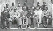 A black and white photo of 13 Christian Zulu men seated outside of a church.