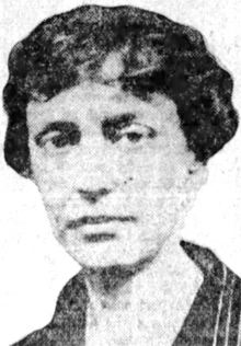 A white woman with short dark wavy hair, wearing a collared shirt