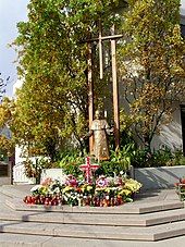 Statue of man in robes in front of a large cross.