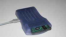 Photo of a blue colored device with a large slot in front, and a cable is attached to the device