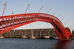 A red, twisting bridge spans a canal.