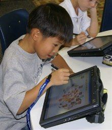 A young Asian boy in a gray T-shirt at a round table using a tablet computer