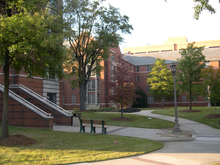 A red brick and white concrete, four-story apartment building with a landscaped courtyard in the foreground