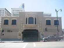 Color photograph of a two-story building. The main entrance has an awning and double doors. Above the entrance on the second story is an ornate bay window. On either side of the bay window there are smaller windows with balconets.